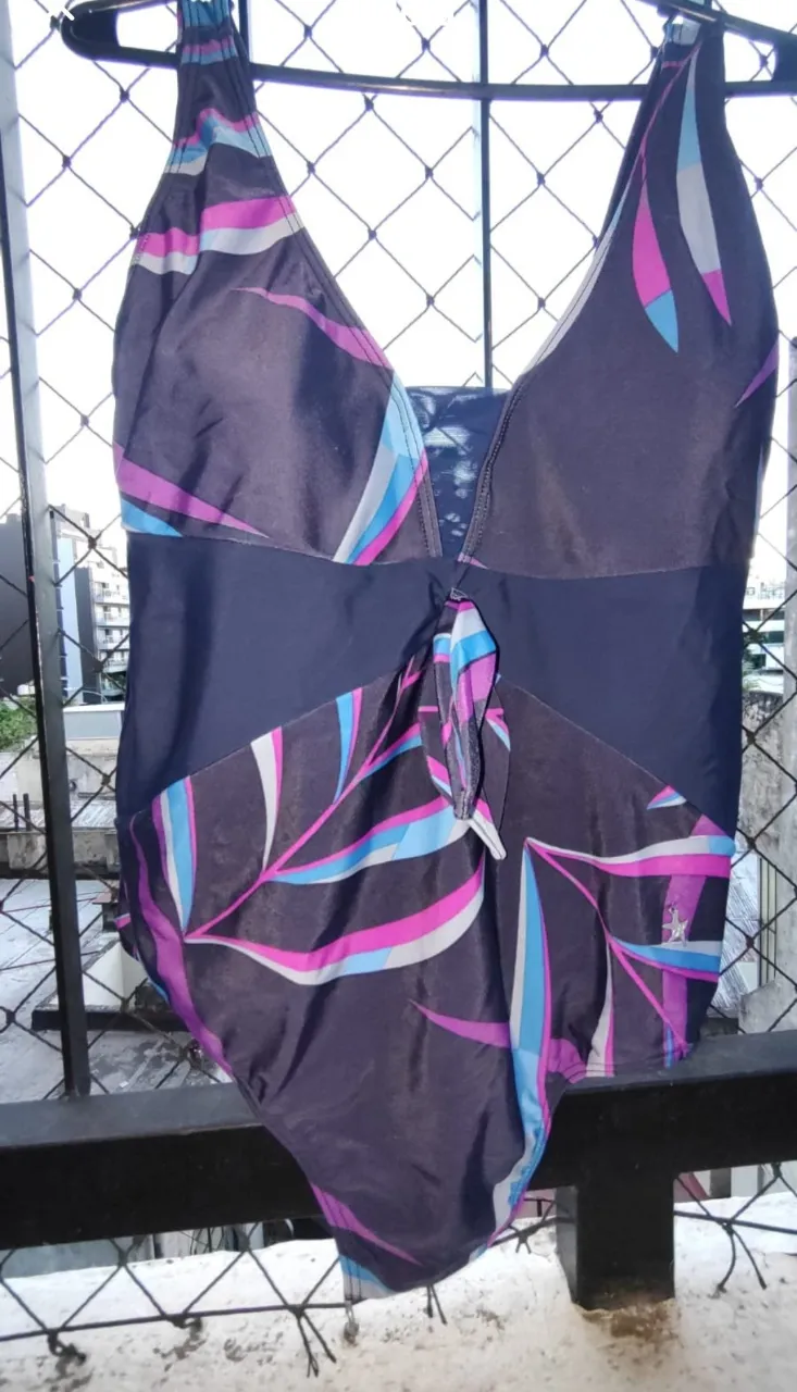 Traje de baño entero estampado con hojas en tonos fucsia, azul y gris sobre fondo oscuro. Posee un lazo en la parte delantera y breteles finos.

En el pecho tiene dos detalles que la hacen única. En el pecho una ventana de tull azul, y en el bajo busto un frunce. 
En el busto tiene taza, SIN ARO. 

Es talle 50 y sus medidas son:
Largo total de la malla: 69 cm 
Ancho de Sisa 43 cm
Ancho de cadera 46 cm 