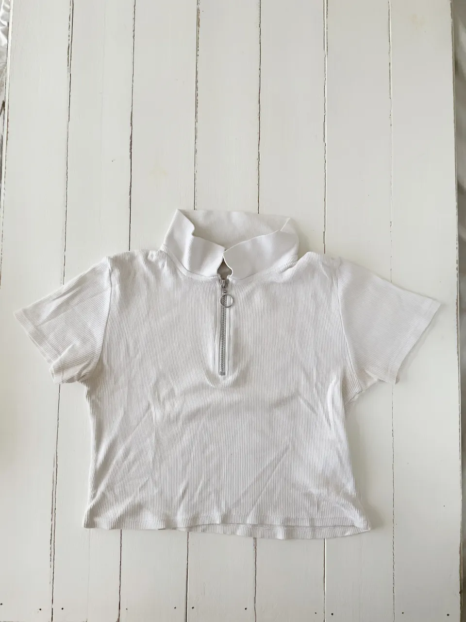 Remera blanca de manga corta con cuello tipo polo y cierre metálico al frente.