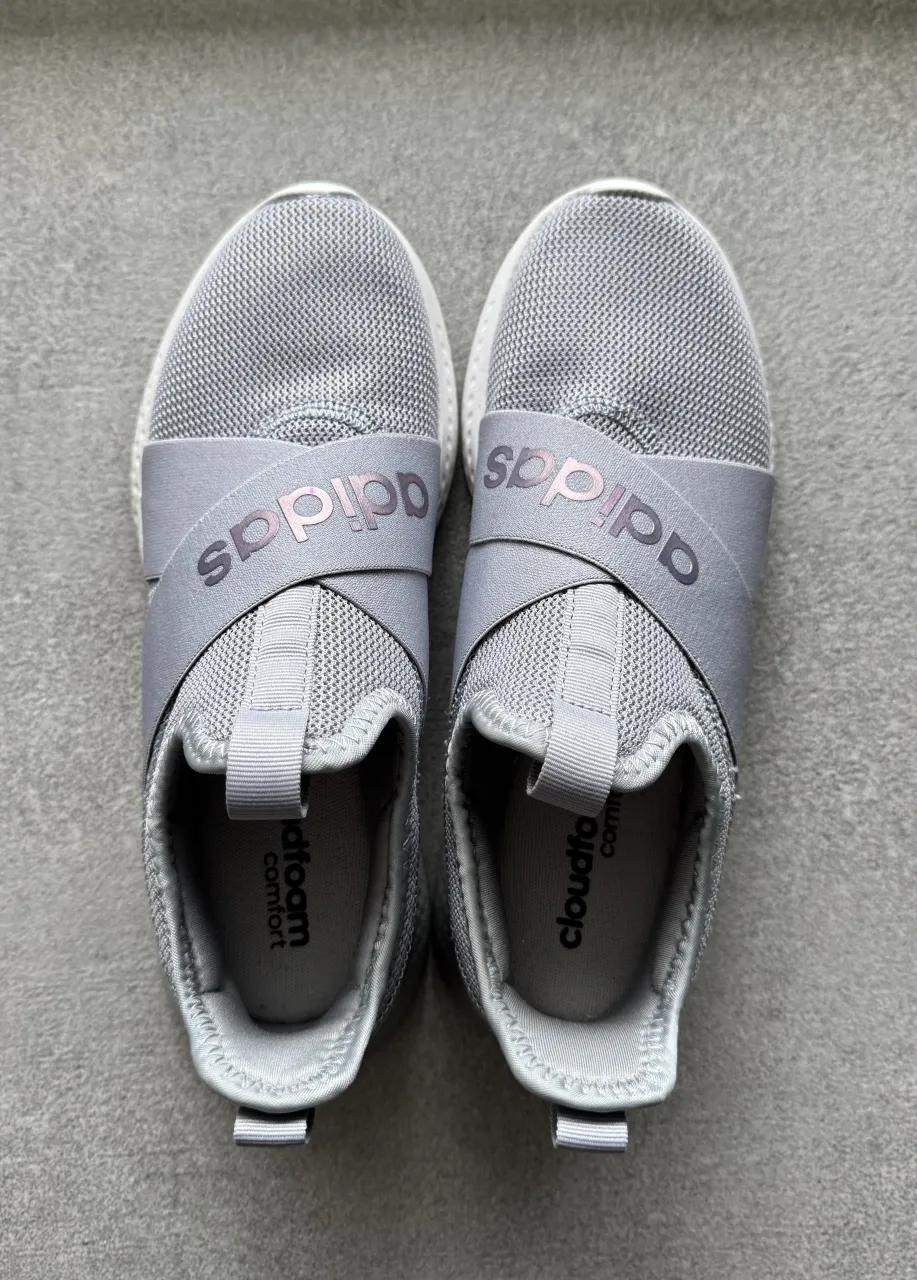 Zapatillas deportivas Adidas, color gris, sin cordones, con banda elástica cruzada en el empeine con el logo de la marca. Ideales para entrenar o para un look casual y cómodo.