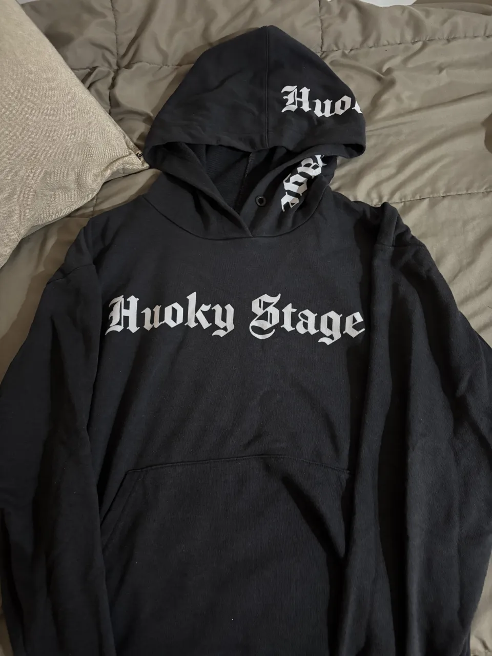 Buzo canguro negro con estampa "Huoky Stage" en blanco. Diseño oversize con capucha y bolsillo frontal. Ideal para un look urbano y canchero.