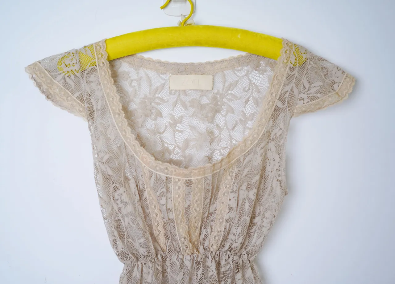 Remera larga de encaje color beige con mangas cortas y escote redondo. Posee elástico en la cintura.