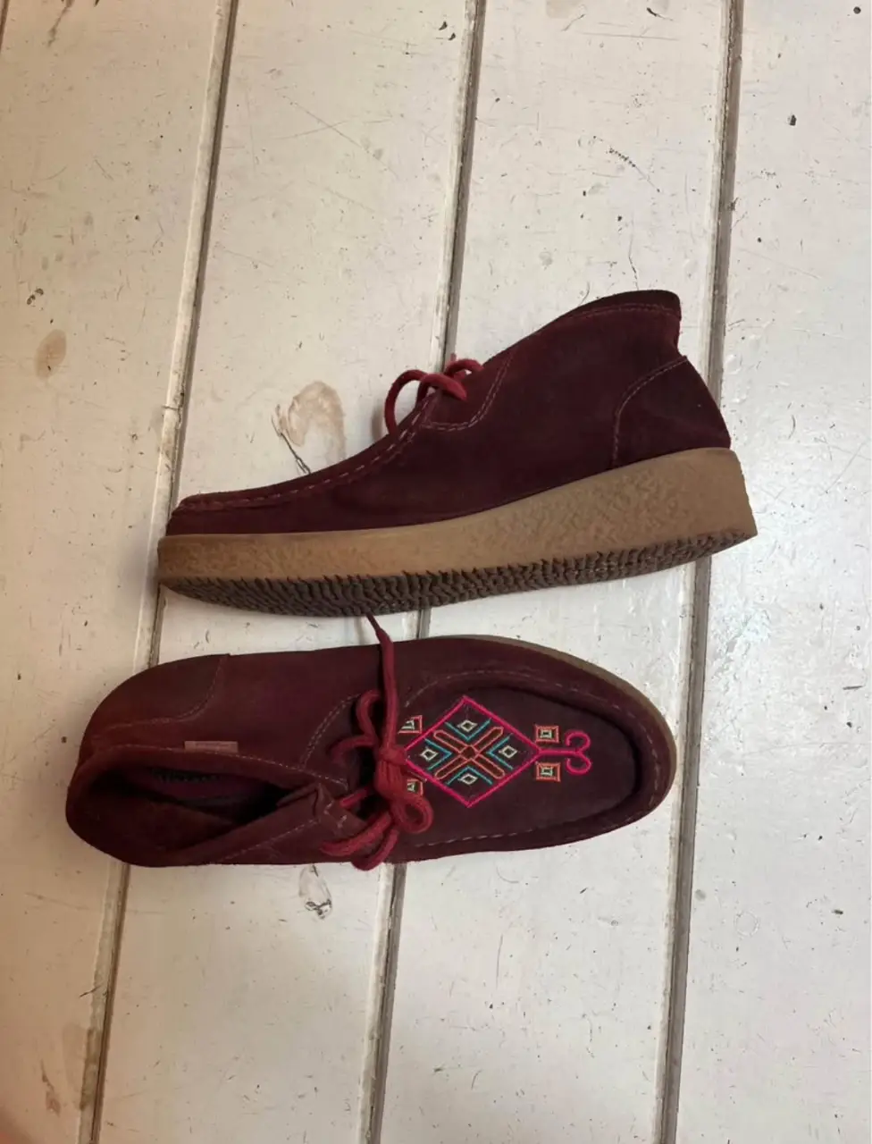 Zapatos tipo mocasín de gamuza color borgoña con detalles bordados en la parte superior. Suela de goma color beige. Estilo vintage y artesanal.