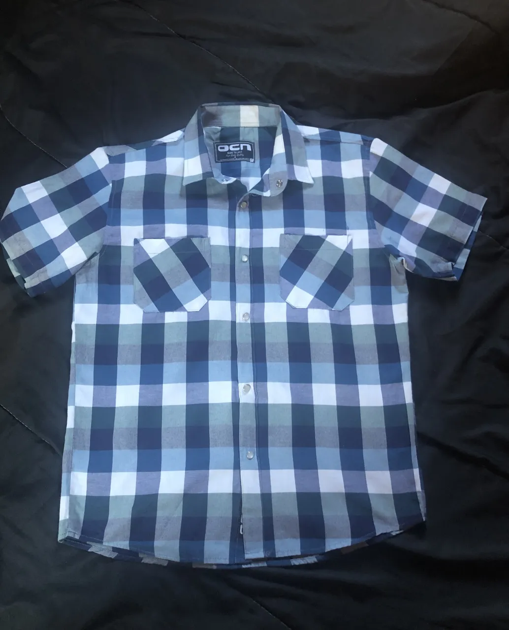 Camisa a cuadros de manga corta con dos bolsillos en el frente. La camisa tiene botones al frente y en los bolsillos.