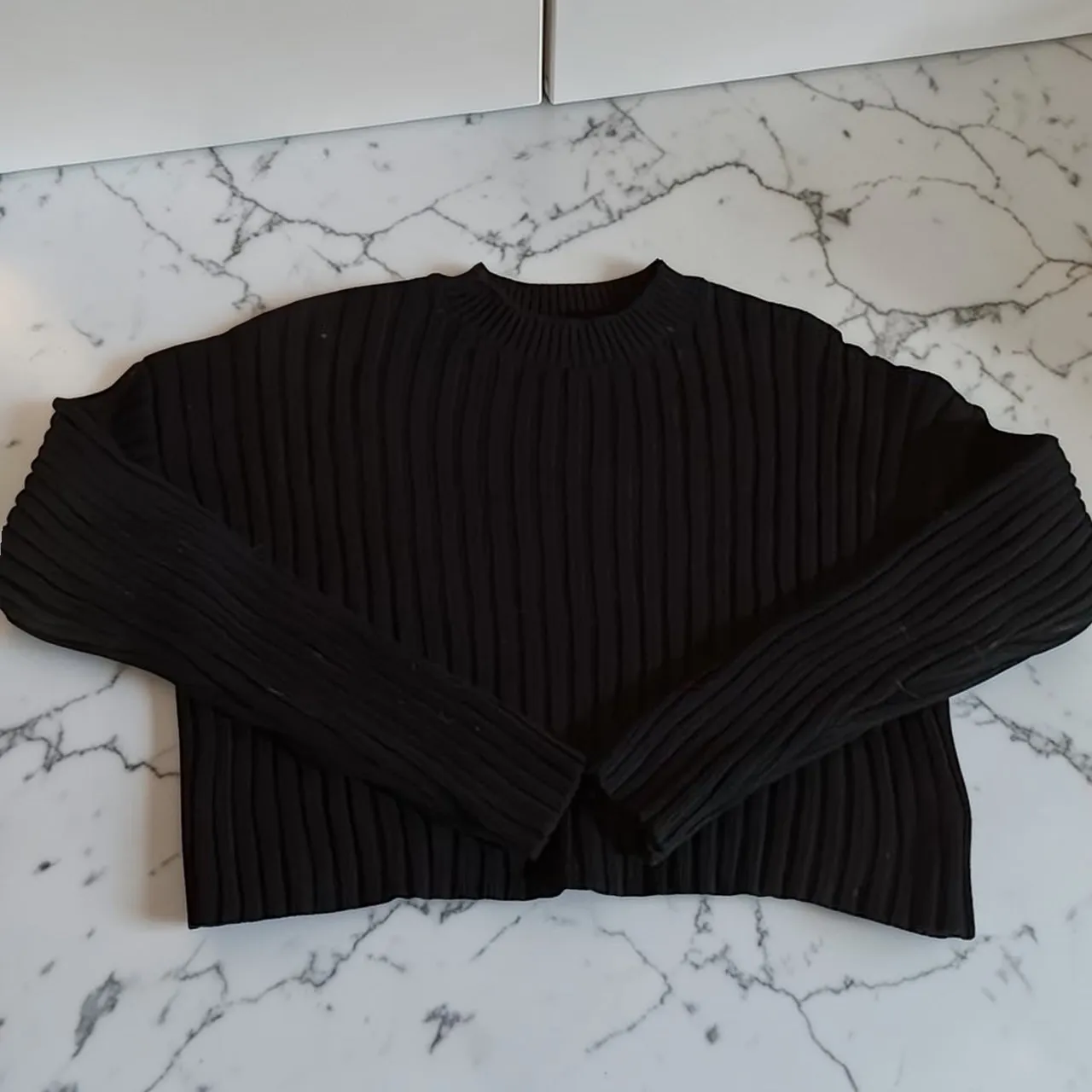 Sweater negro de tejido acanalado con cuello redondo y mangas largas.