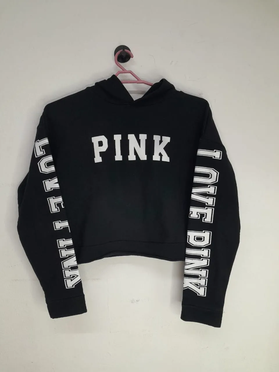 Buzo negro crop con capucha. Estampado blanco en el frente con la palabra "PINK". Las mangas tienen estampadas las palabras "LOVE PINK" en blanco.
