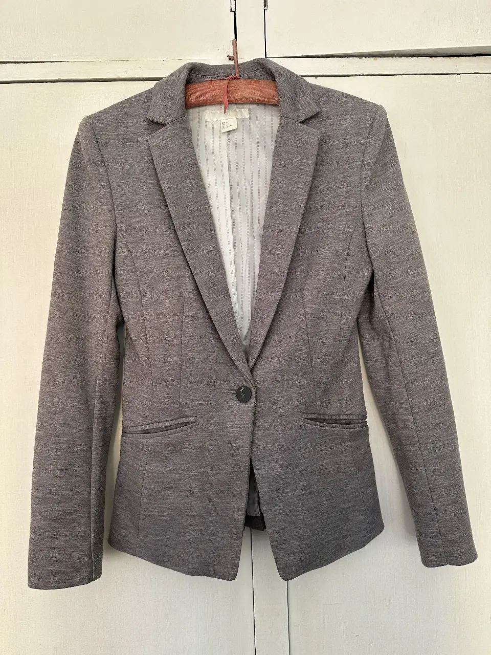 Blazer gris de mujer, entallado, con un solo botón y bolsillos delanteros. Ideal para un look formal o de trabajo.