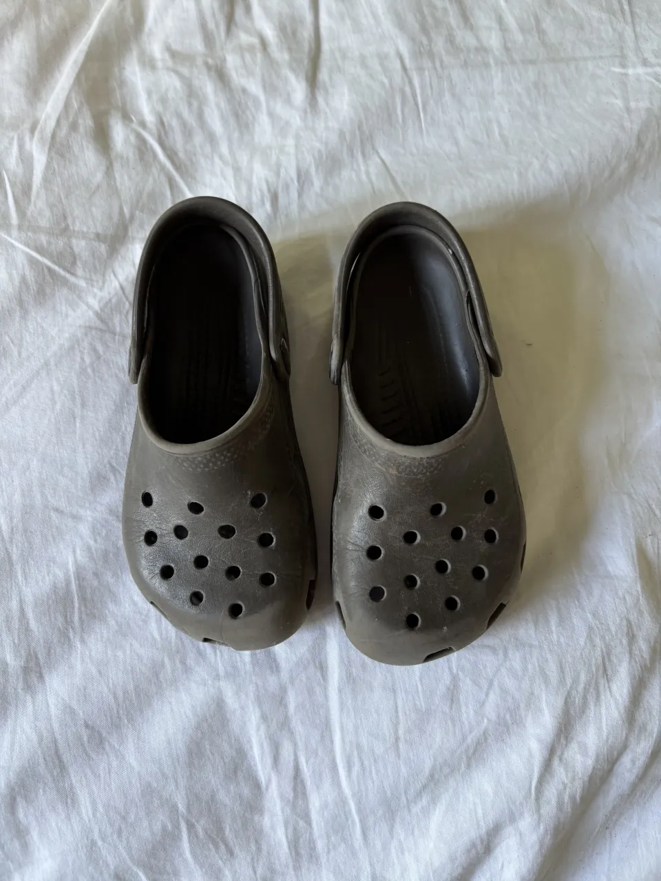 Ojotas de goma color marrón. Tienen la marca 'crocs' grabada en la suela.