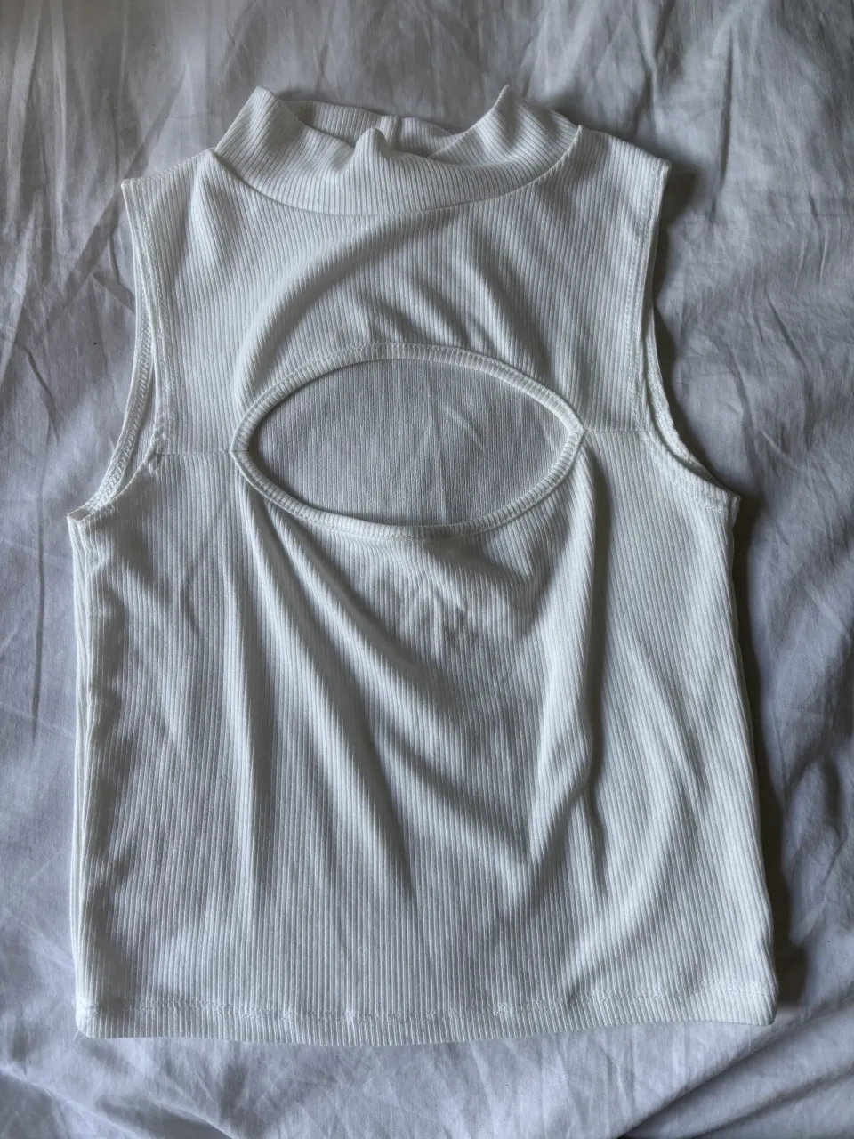 Musculosa blanca con cuello alto y recorte ovalado en el frente.