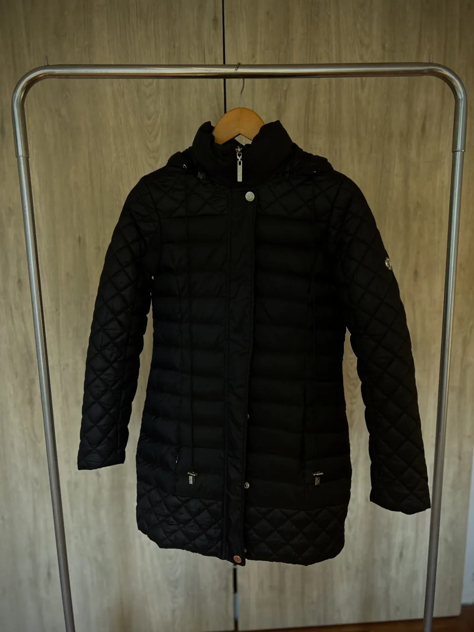 Campera negra acolchada con capucha. Tiene cierre al frente y botones a presión. Posee bolsillos laterales con cierre y un logo circular en la manga izquierda. Marca Perramus