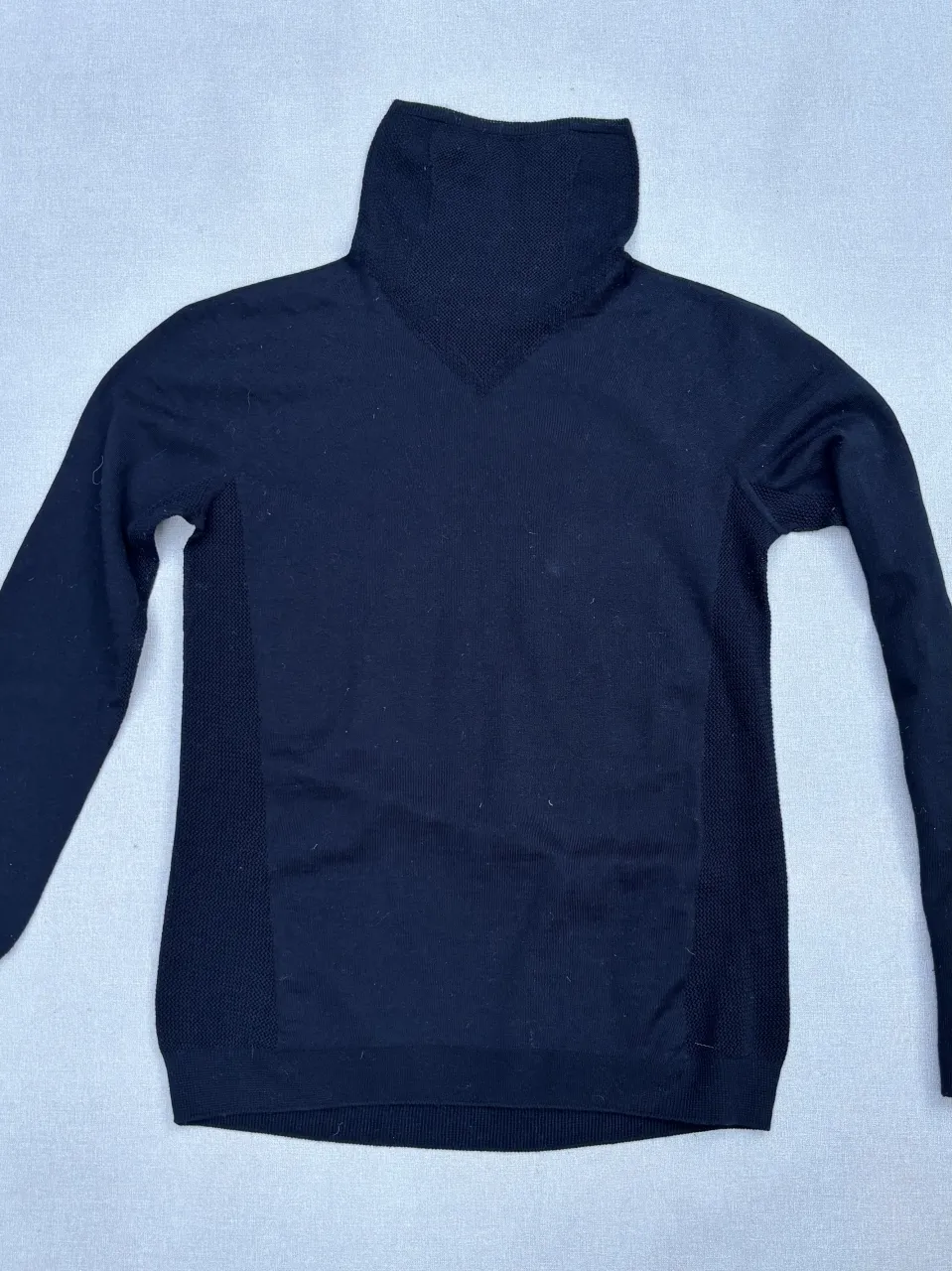 Pulóver negro de cuello alto con detalles de tejido en los laterales y puños con ojal para pulgar. Ideal para un look comfy y casual.