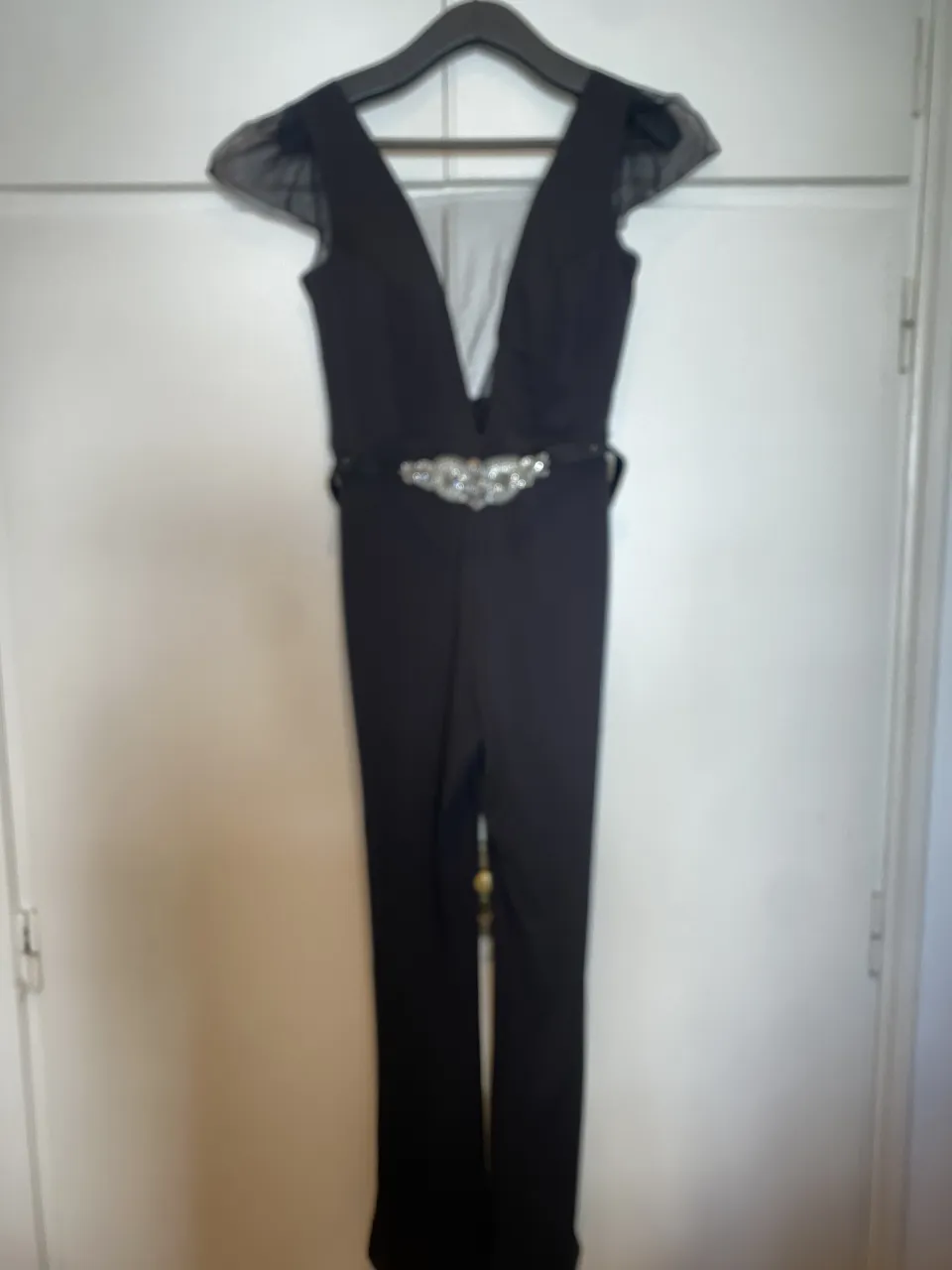 Mono negro de vestir con escote en V profundo, mangas cortas de tul y cinturón con apliques de strass.