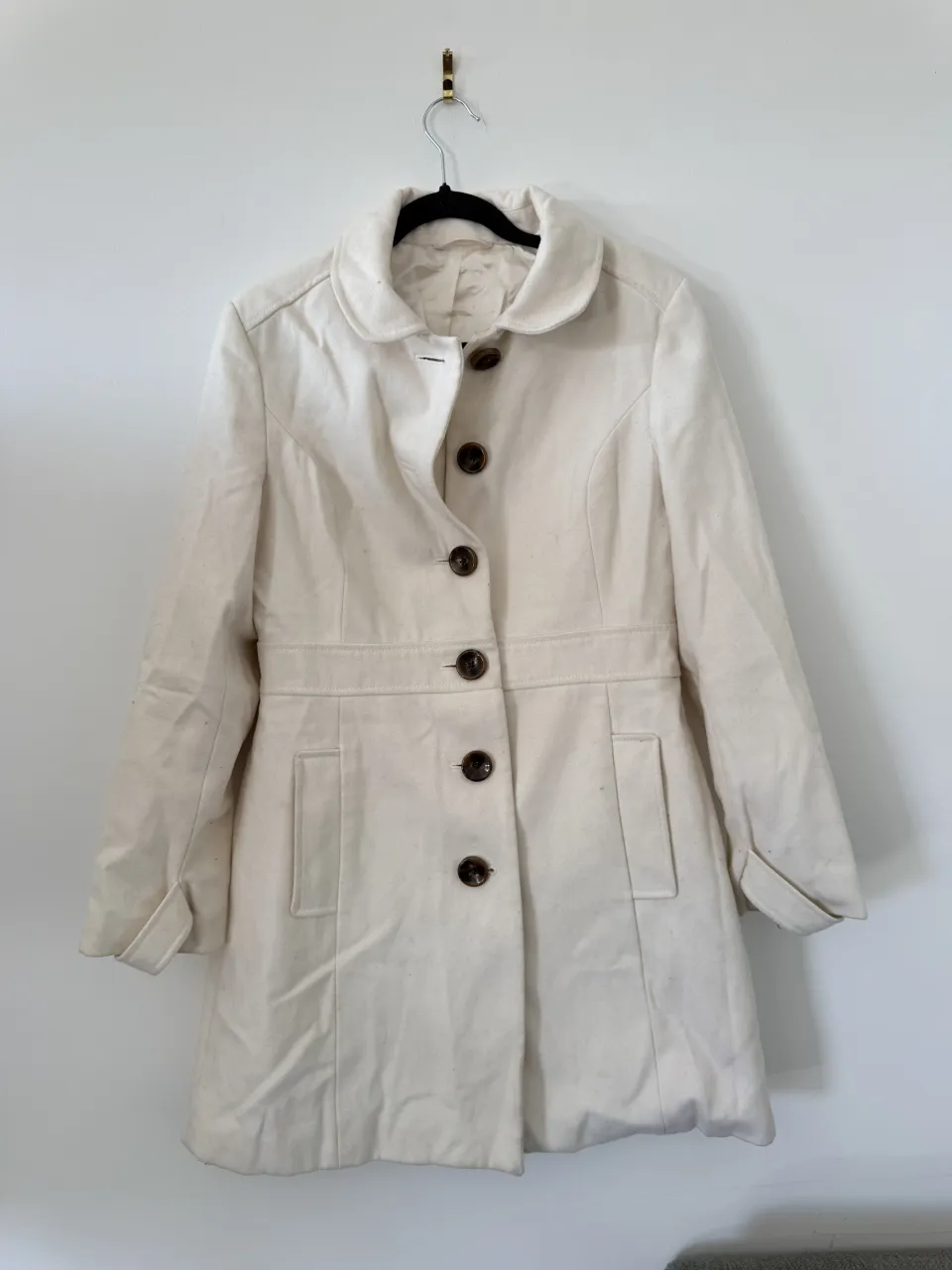 Abrigo peacoat blanco, con botones marrones y cuello redondo. Ideal para un look elegante y casual.
