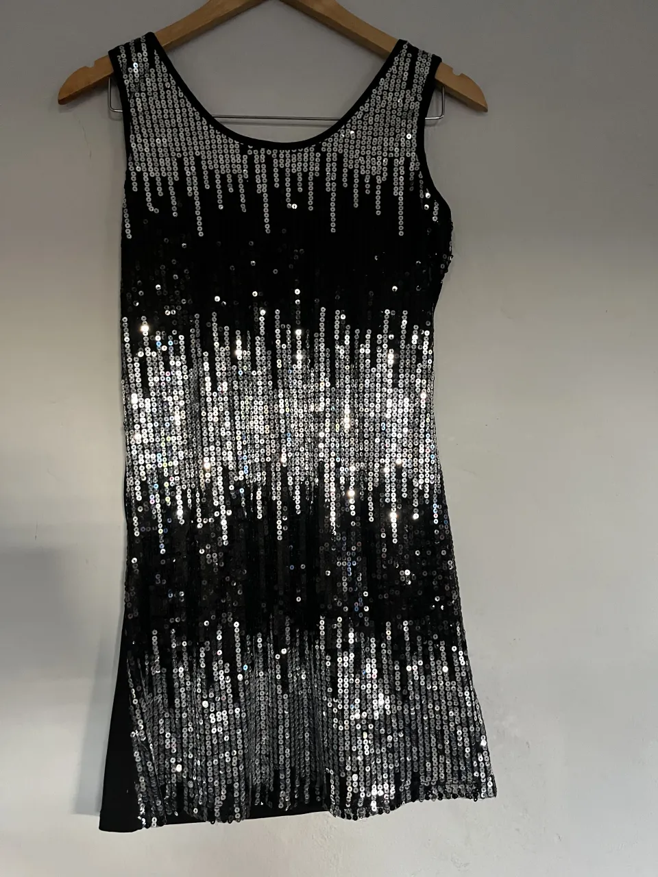 Vestido negro sin mangas con lentejuelas plateadas en la parte delantera. Las lentejuelas forman un diseño vertical que simula una cascada.