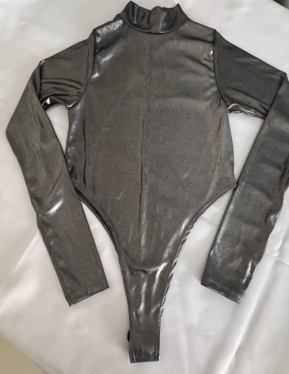 Body de manga larga con cuello alto y terminación tipo colaless. Posee un acabado brillante.