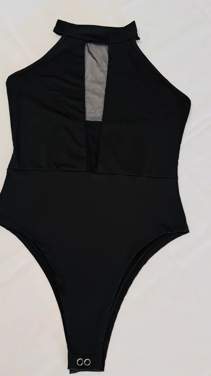 Body negro con cuello alto y detalle de tela de red en la parte delantera del escote. Posee broches en la parte inferior.
