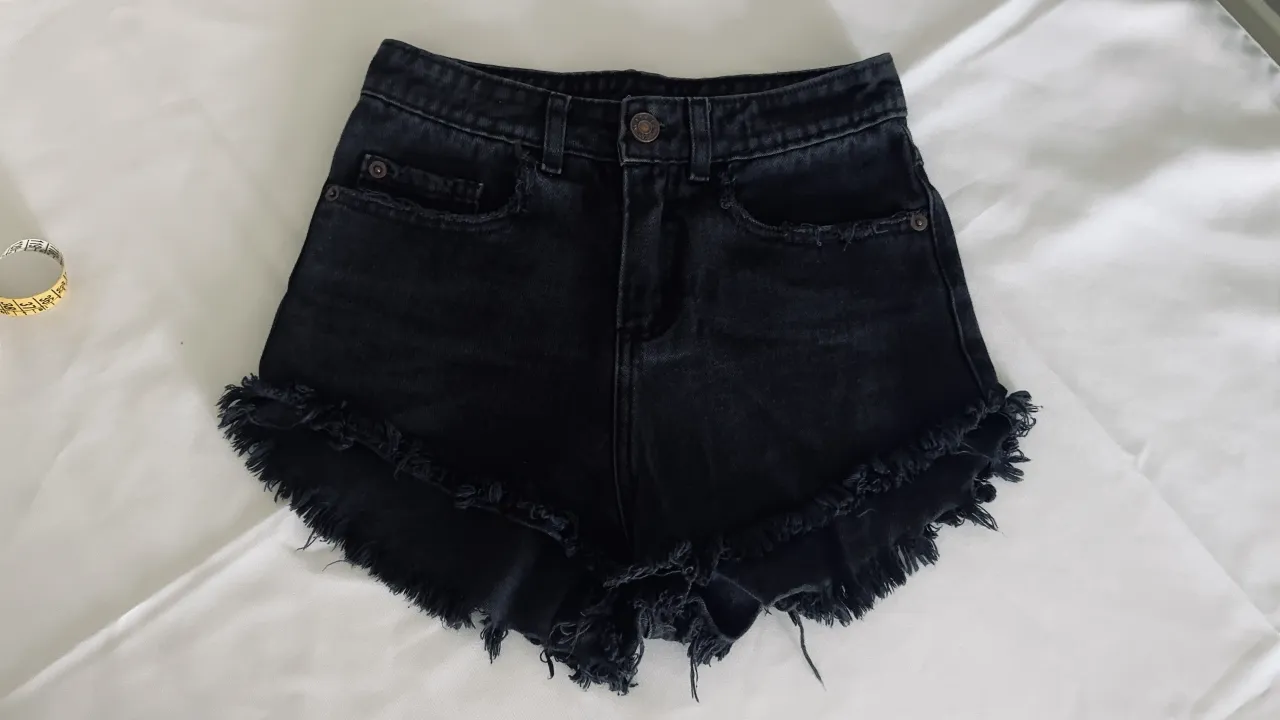Shorts de jean negros con roturas y flecos en el ruedo.