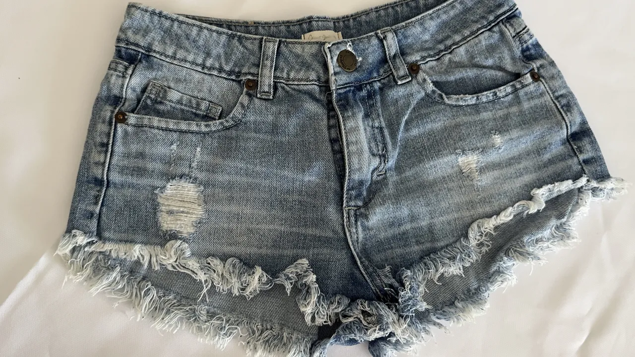 Shorts de jean tiro alto con roturas y detalles desflecados en los bordes. Lavado claro.