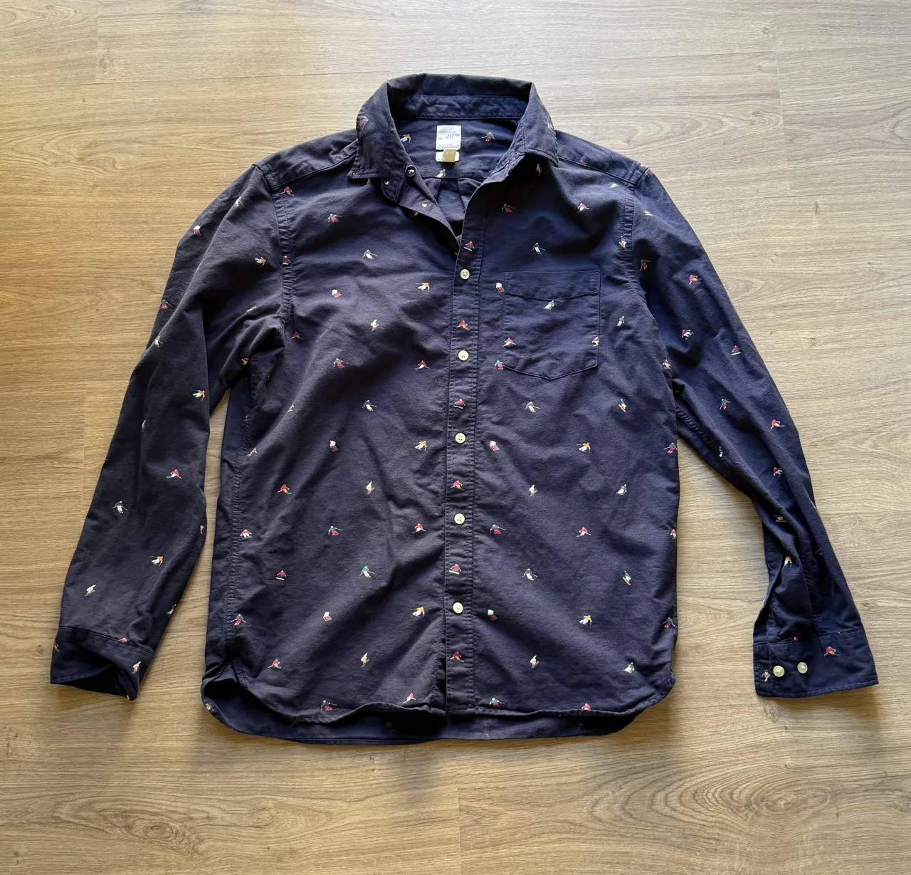 Camisa azul marino de manga larga con estampa de patinadores sobre hielo. Tiene cuello, botones al frente y un bolsillo en el pecho.