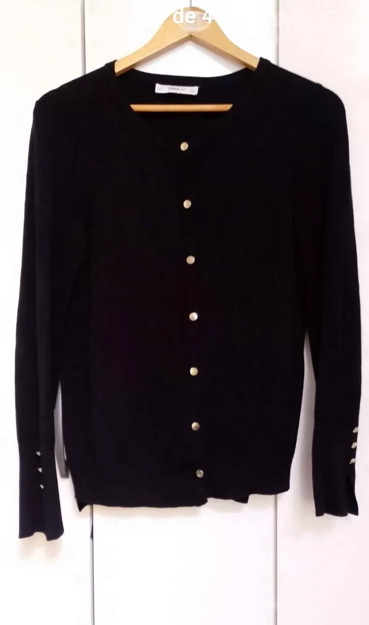 Cardigan negro con botones dorados al frente y en los puños. Cuello redondo.