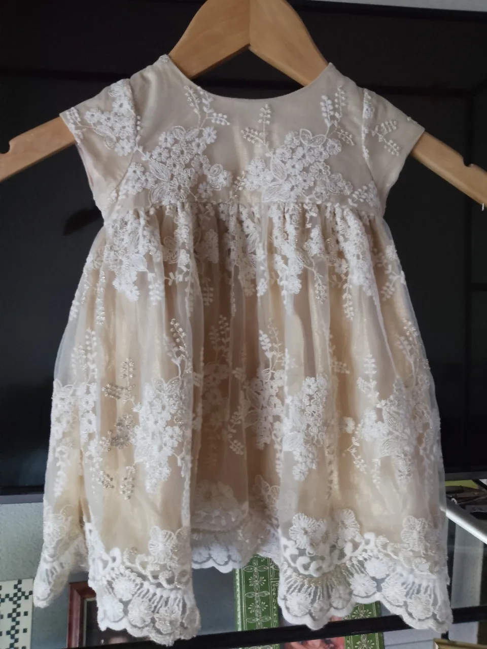 Vestido de bebé color crudo con detalles de encaje blanco y bordados florales. Posee un lazo de satén en la espalda.
