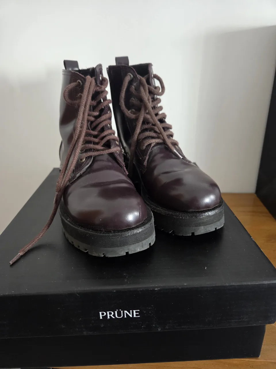 Botas de cuero color borravino con cordones marrones. Tienen suela negra gruesa.