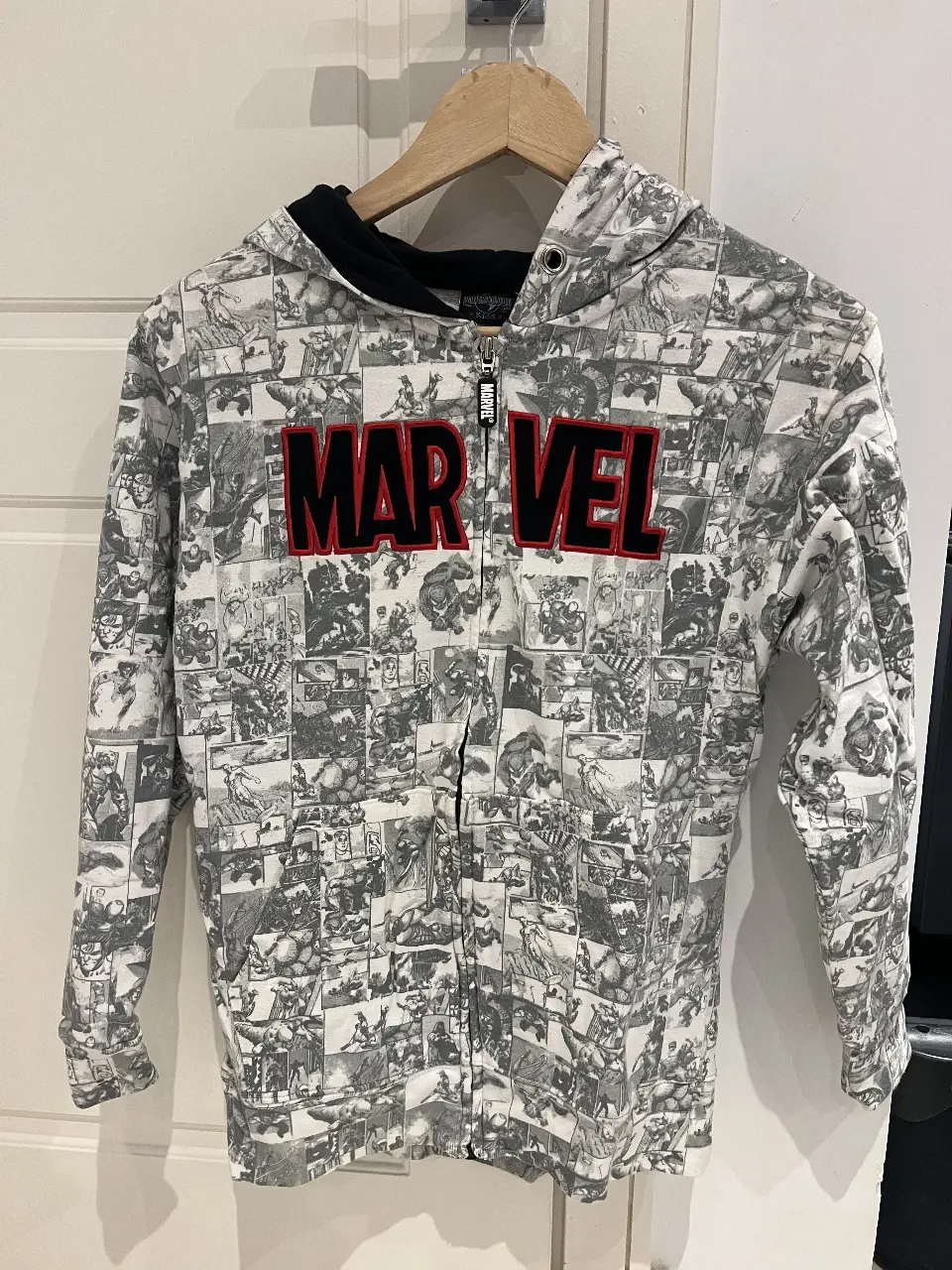 Buzo con cierre para hombre, con estampado de comics de Marvel. El buzo es de color gris con detalles en rojo y negro. Ideal para un look casual y urbano.