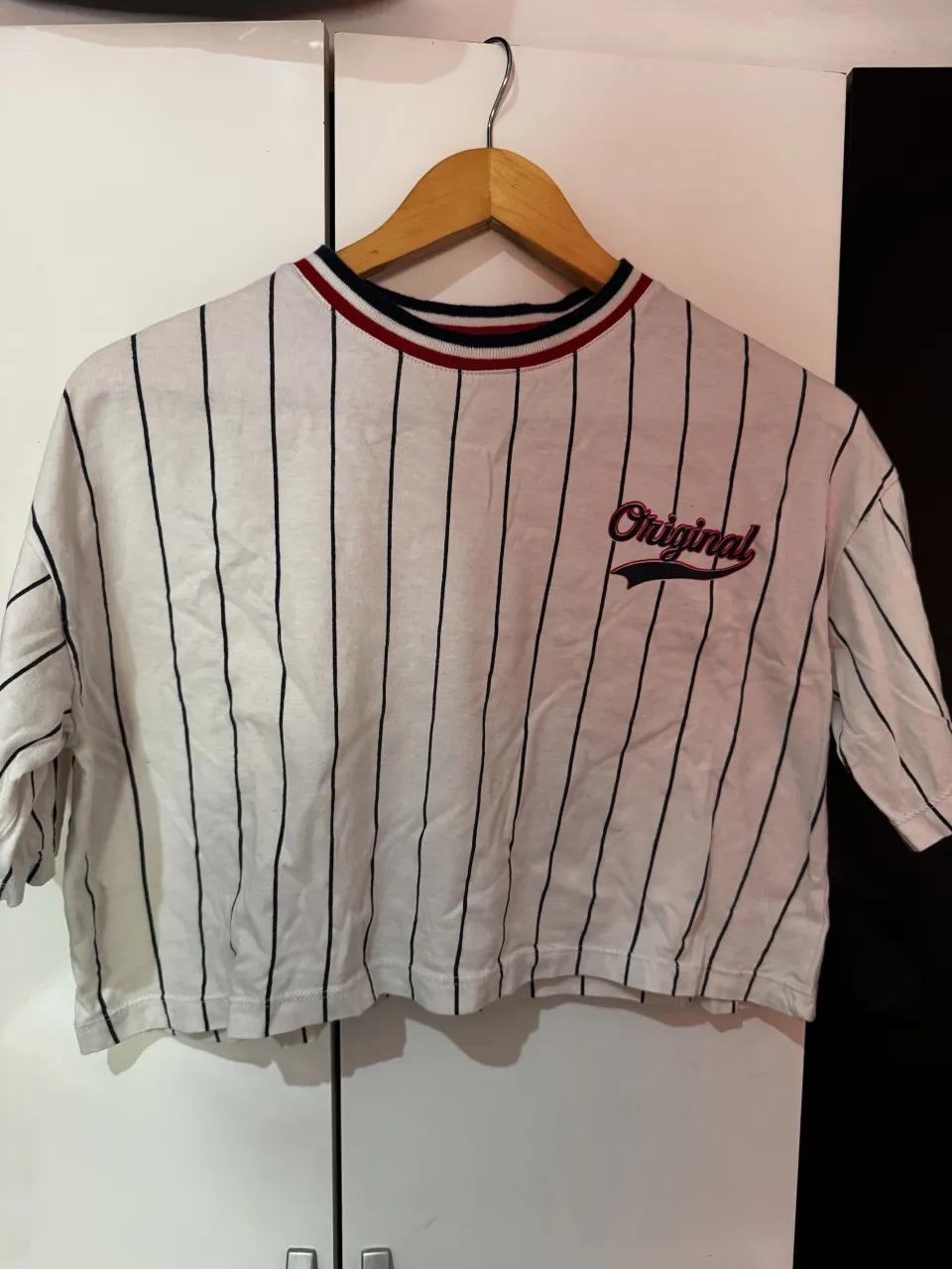 Remera crop top a rayas verticales blancas y negras, con la inscripción "Original 79" estampada en el frente y la espalda. Cuello redondo con detalles en rojo y azul.