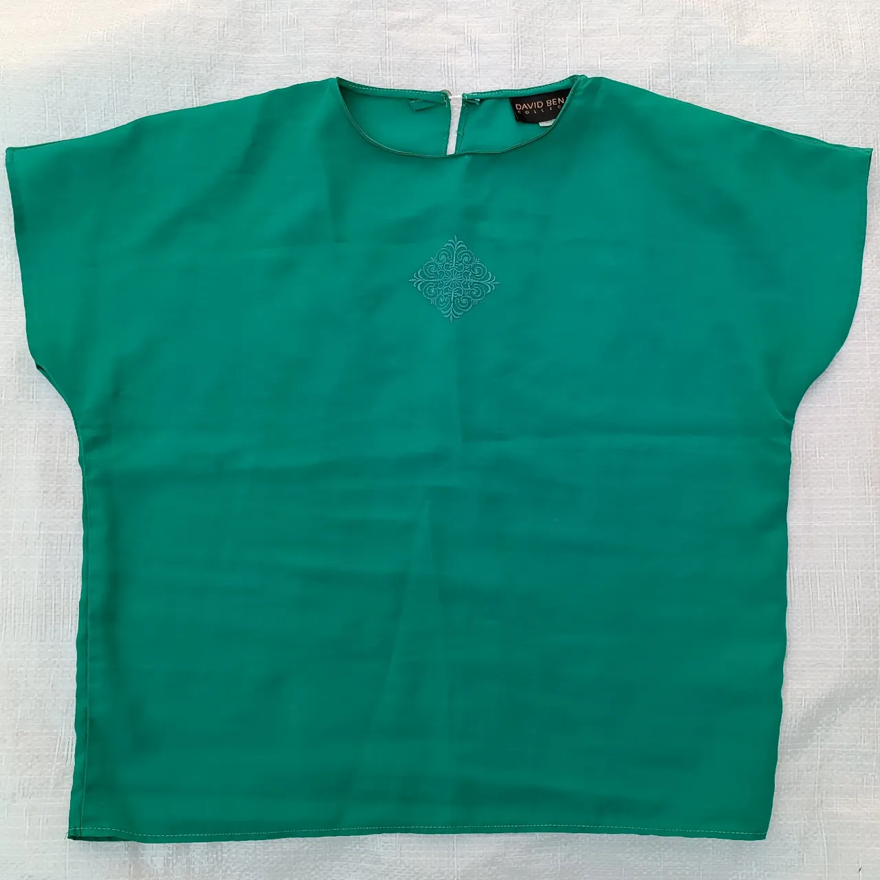 Remera verde esmeralda con bordado central en el frente. Cuello redondo y mangas cortas.
Tiene hombreras.
Tiene desgastada la tela traslúcida a los costados.

MARCA: DAVID BENJAMIN COLLECTION
100% poliester

MEDIDAS:
Contorno de busto (110cm.)
Contorno de cintura (100cm.)
Largo (55cm.)
made in usa