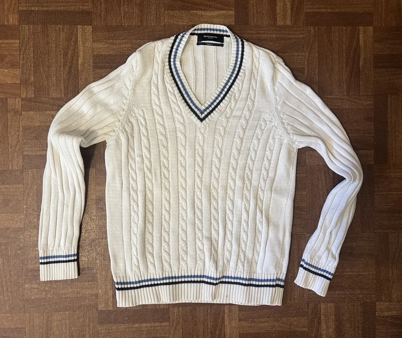Sweater de tejido de punto blanco. TALLE S. Posee cuello en V con detalles de rayas azules y negras. Ideal para un look casual y cómodo.