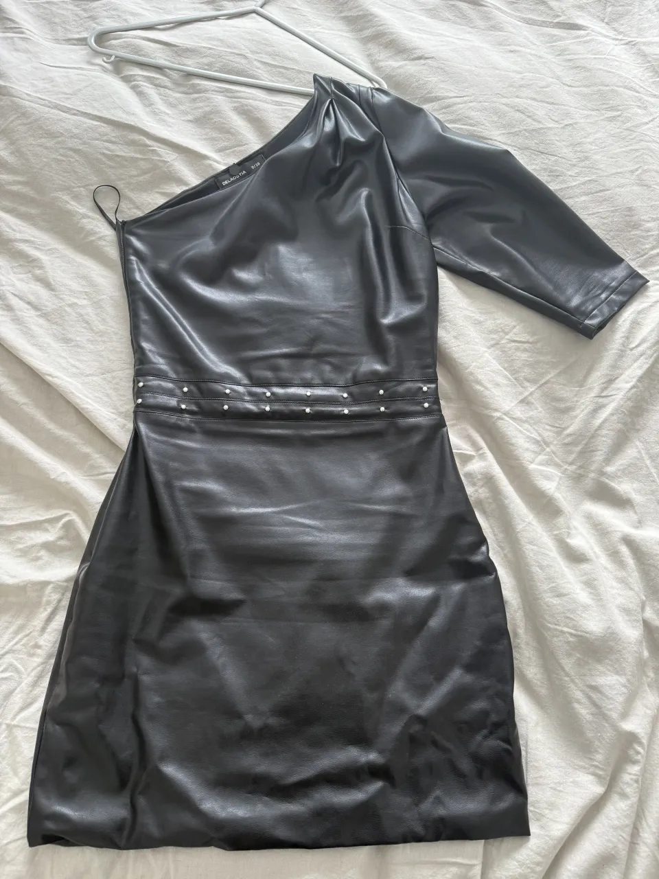 Vestido negro de cuero sintético, con un solo hombro y manga hasta el codo en un lado. Posee detalles de tachas plateadas en la cintura. Es talle 38, está en perfecto estado😊