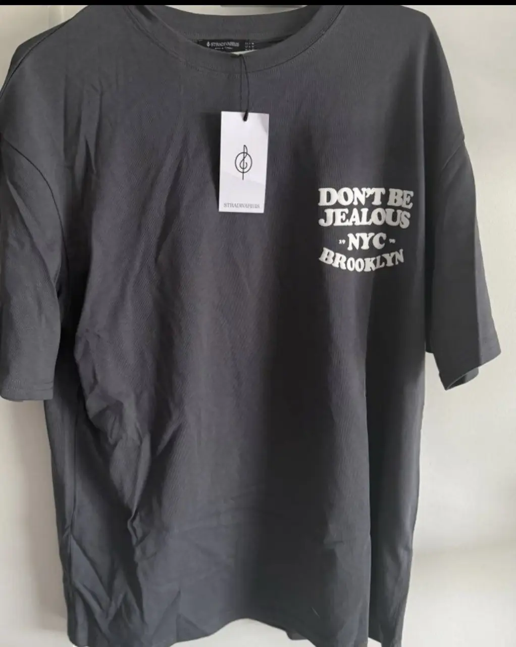 Remera gris de hombre con estampado "Don't be jealous - NYC - Brooklyn" en la espalda. De la marca Stradivarius, talle M. Ideal para un look casual y urbano.