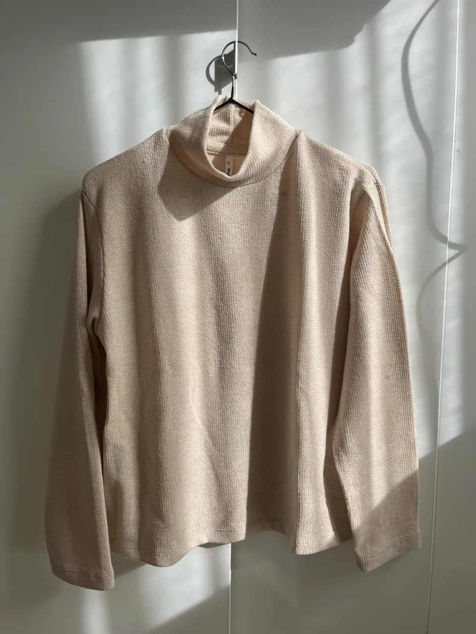 Sweater de cuello alto en color crudo, con un tejido sutilmente brillante. Ideal para un look casual y elegante, perfecto para los días frescos de otoño o invierno. Su diseño atemporal lo hace versátil para combinar con diferentes prendas.