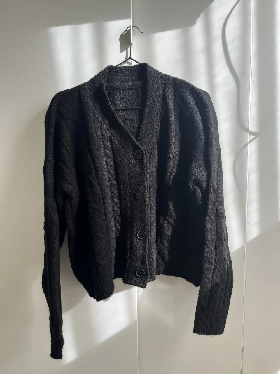 Cardigan de lana negro con botones y trenzas. Un clásico que no puede faltar en tu guardarropa.