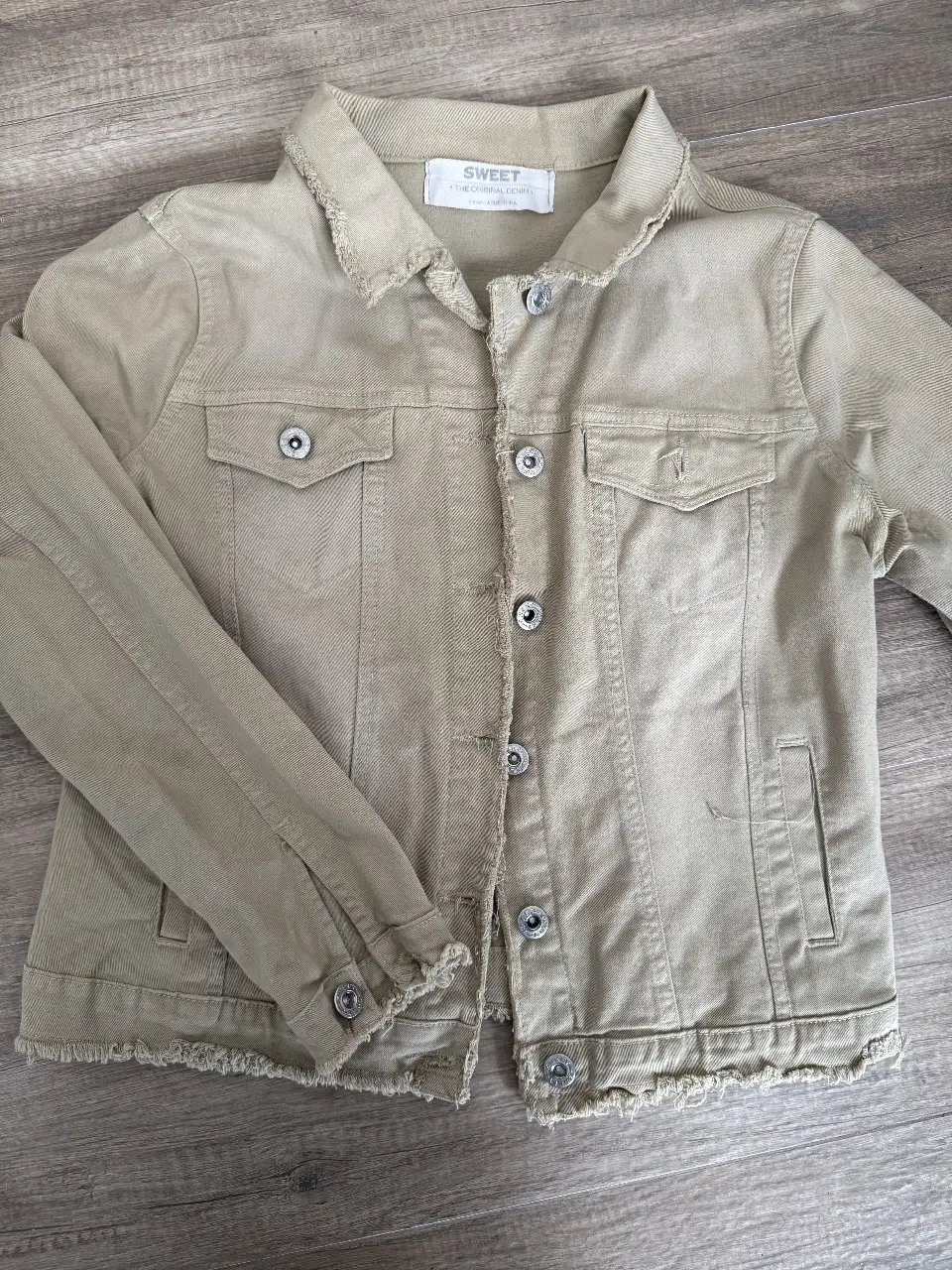 Campera de jean color khaki, con detalles desflecados en el bajo y cuello. Posee bolsillos delanteros y botones metálicos. Ideal para un look casual y canchero.