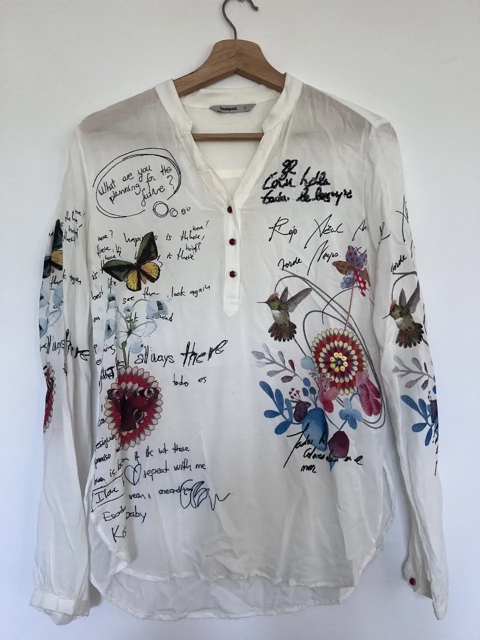 Blusa Desigual blanca con estampado de flores, mariposas y frases manuscritas. Detalles de lentejuelas en el cuello. Talle S.