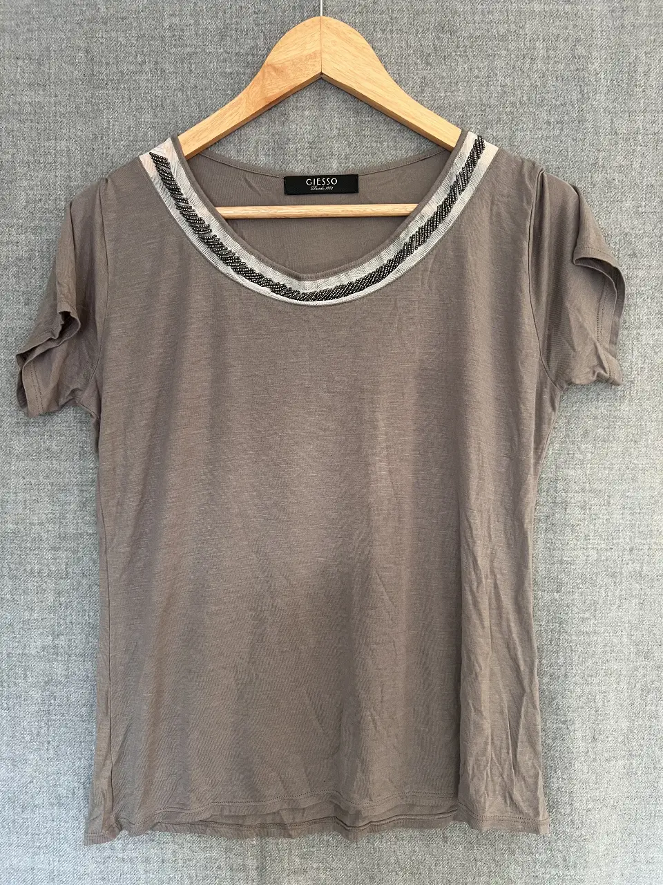 Remera de mujer color gris con cuello redondo adornado con detalles bordados en blanco y negro. Ideal para un look casual y cómodo.