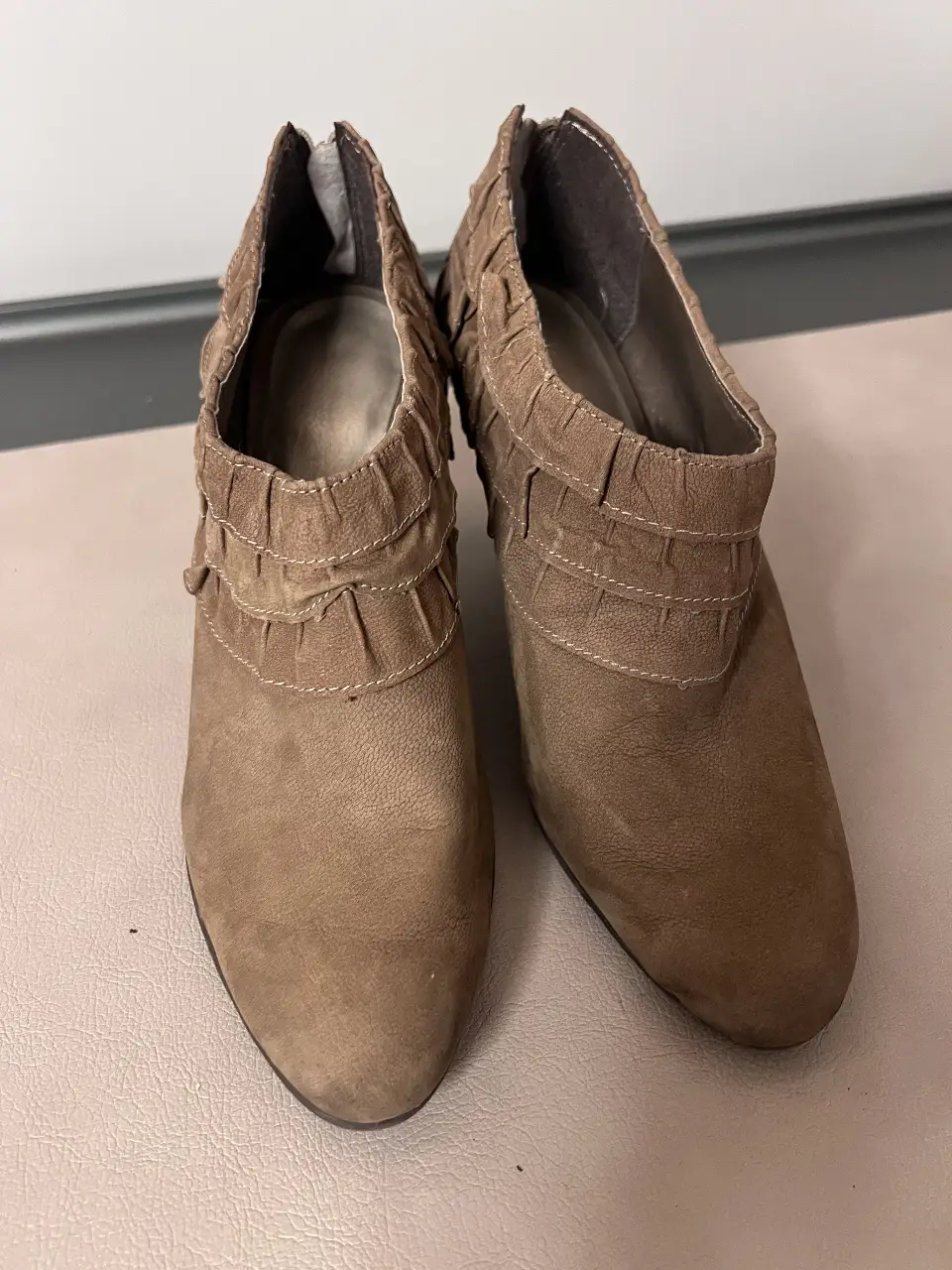 Botas cortas de gamuza marrón con detalle de volados en el borde superior y cierre en la parte trasera. Ideales para un look elegante y sofisticado.