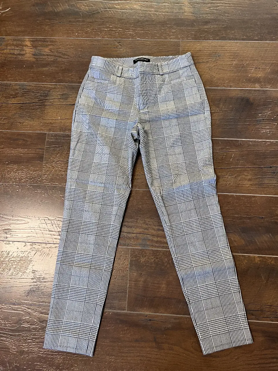 Pantalón sastrero de mujer, con escoces a cuadros en tonos grises y blancos. Corte recto, tiro medio y cierre con botón y cremallera. Ideal para un look formal o de oficina.