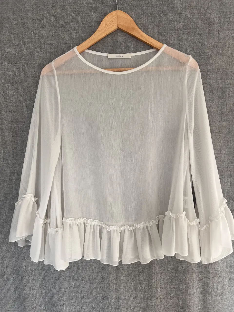 Blusa blanca de gasa con mangas largas y volados en los puños y el ruedo. Ideal para un look elegante y fresco.