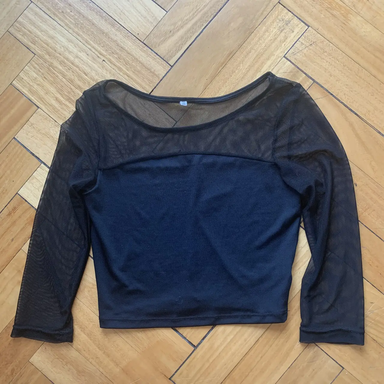 Top negro de manga larga con paneles de malla transparente. Ideal para un look moderno y audaz. Perfecto para combinar con jeans o faldas.