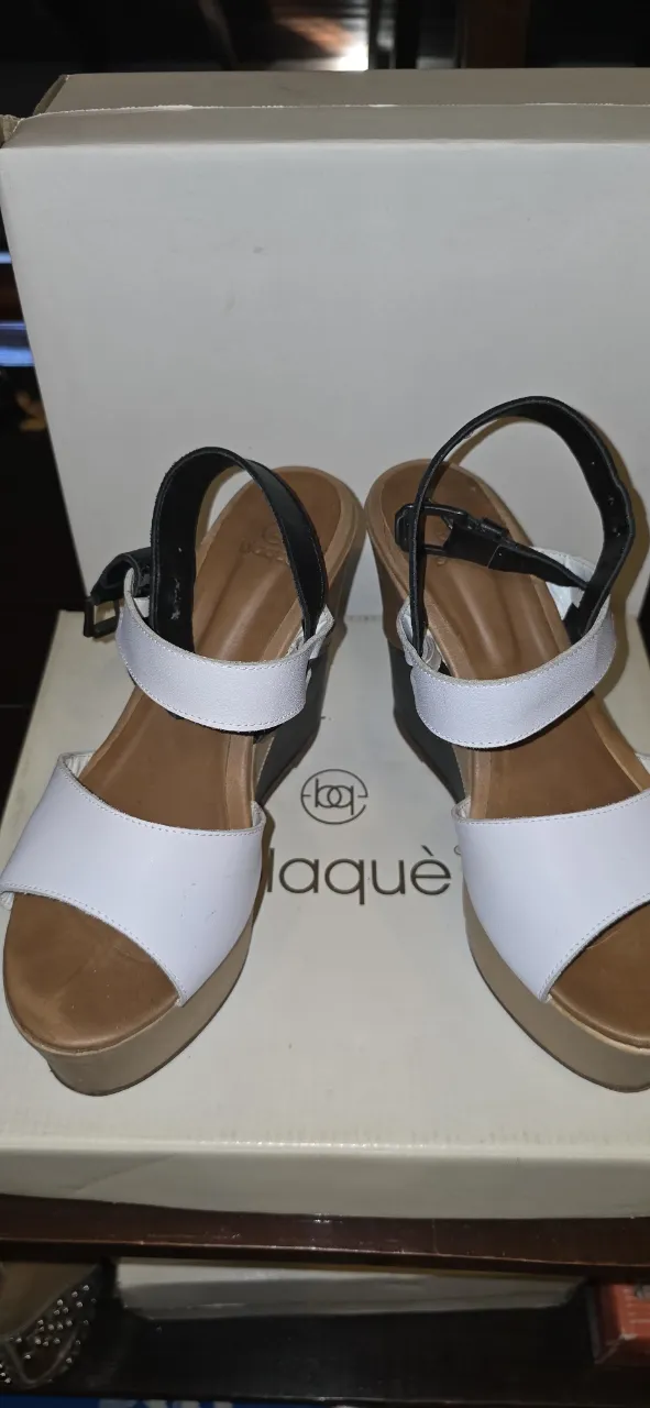 Sandalias de plataforma con tiras blancas y negras, y detalles en color suela y negro en la cuña.