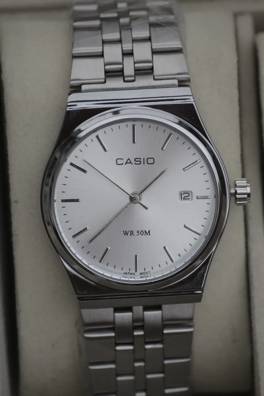 Reloj Casio con malla y caja de acero inoxidable. Esfera plateada con números y fecha.
