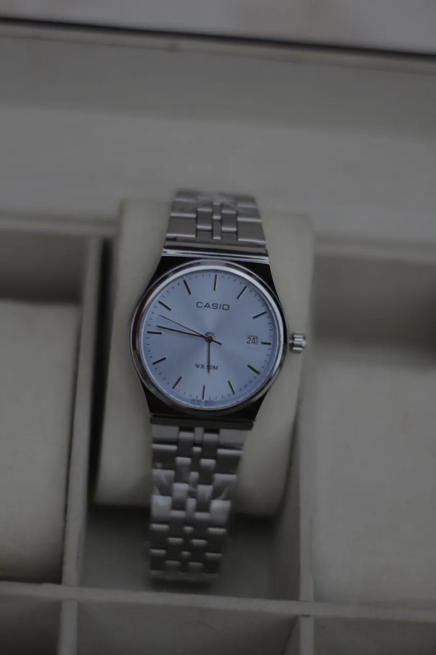 Reloj Casio con malla y caja de acero inoxidable. Esfera redonda de color celeste con detalles plateados. Posee fechador.