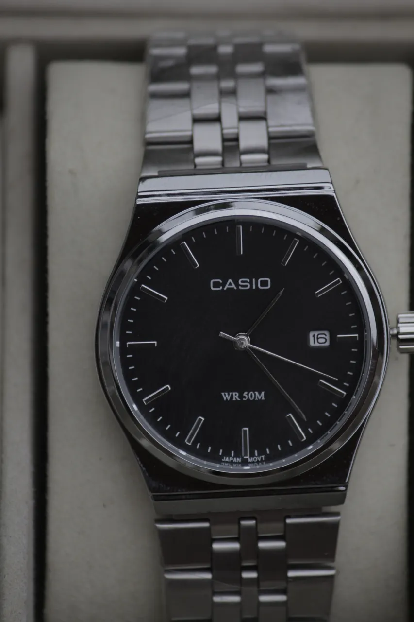 Reloj Casio con malla y caja de acero inoxidable. Esfera negra con índices plateados y fechador a las 3. WR 50M.