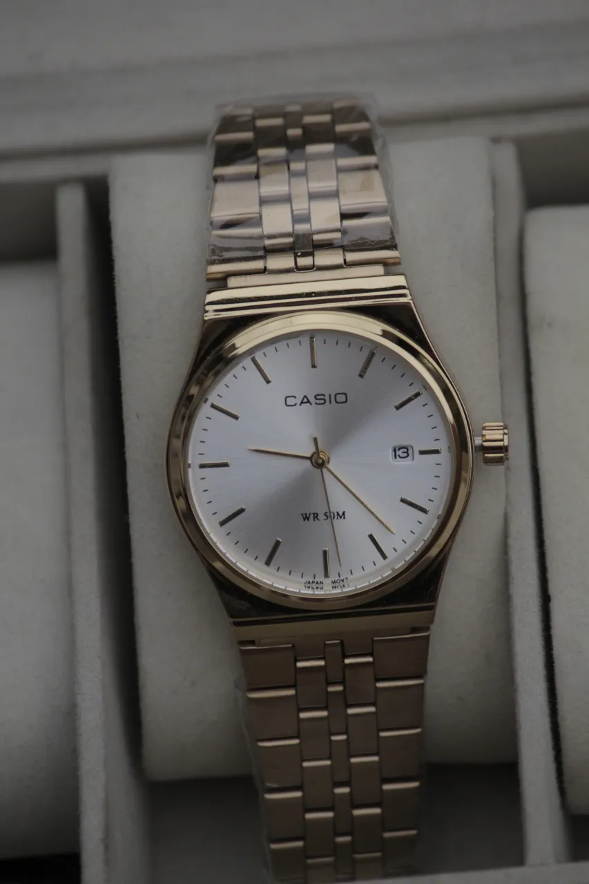 Reloj Casio con malla y caja dorada. Esfera blanca con agujas e índices dorados. Resistente al agua 50 metros.