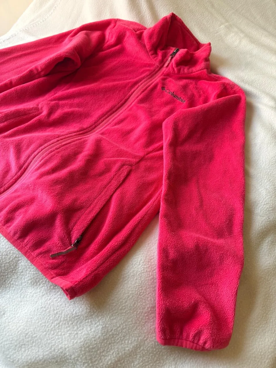 Campera de friza rosa con cierre completo y cuello alto. Tiene dos bolsillos frontales con cierre y el logo de la marca bordado en el pecho.