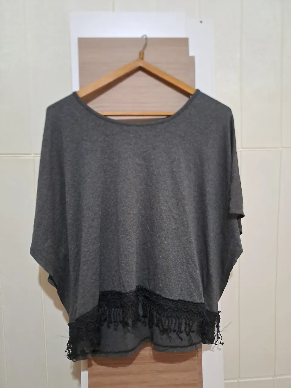 Remera gris con mangas cortas escondidas y detalles de encaje negro con flecos en el borde inferior.