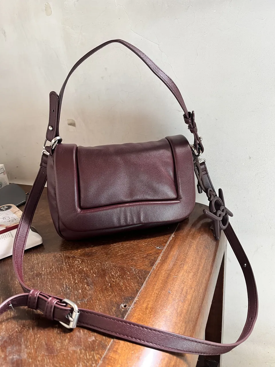 Bolso de cuero color bordó con tapa y cierre interno. Posee un dije colgante con el logo de la marca.