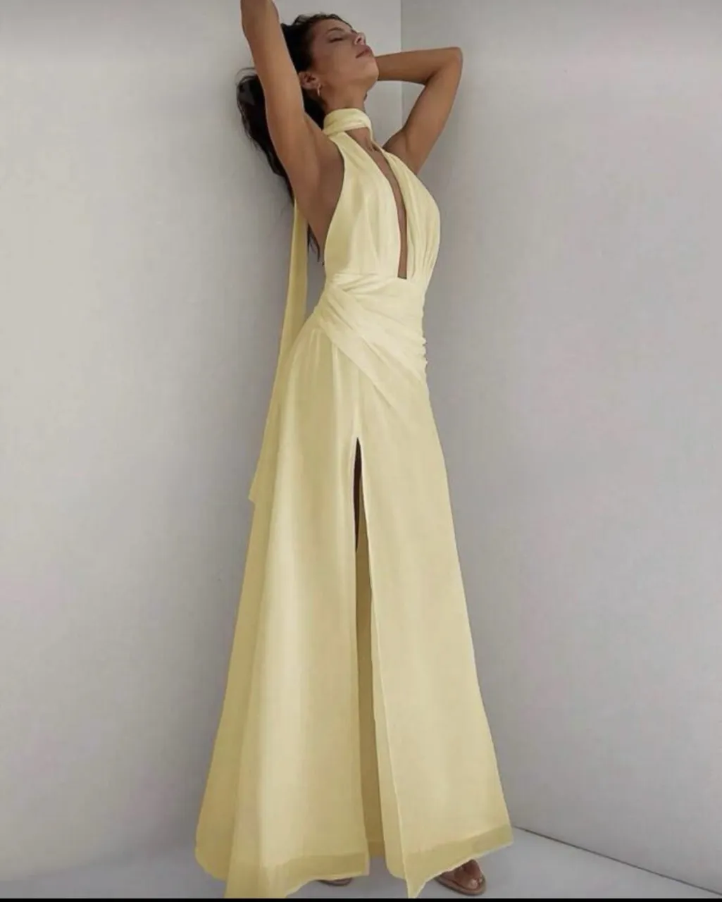Vestido largo amarillo con escote pronunciado en V, tiras finas que se anudan en el cuello y espalda descubierta. Posee una abertura lateral en la falda.