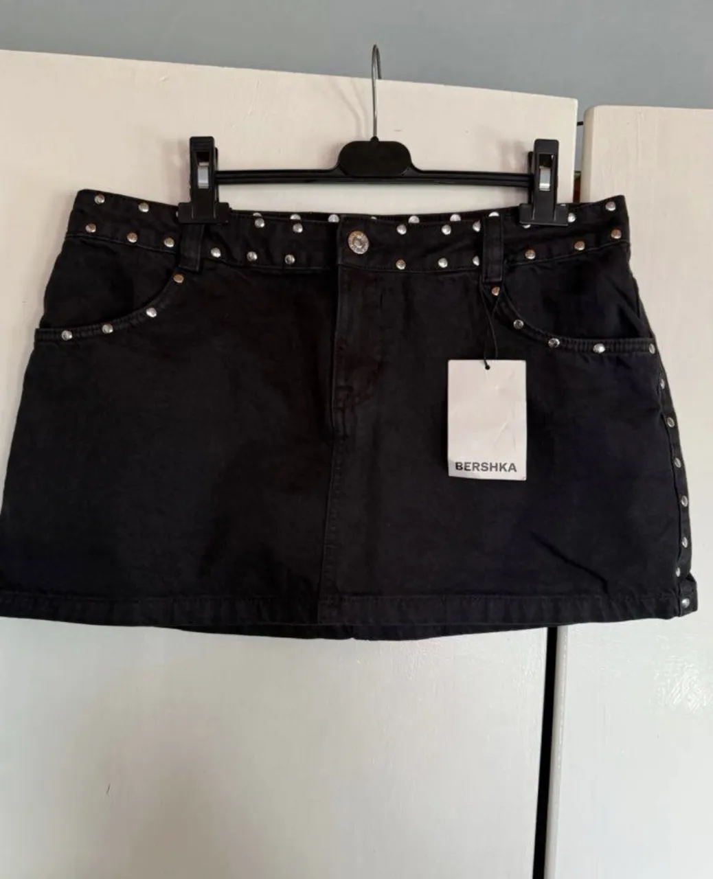 Pollera de jean negra corta con tachas plateadas alrededor de la cintura y en los laterales. Tiene bolsillos delanteros y traseros.